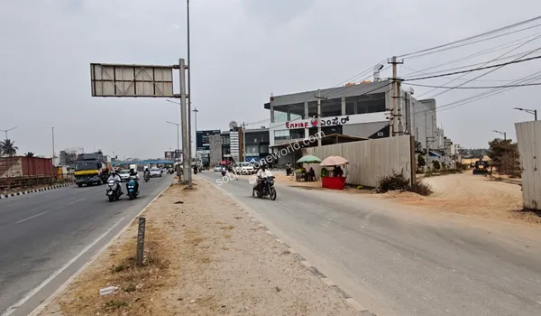 The immediate environment flanking the entrance pathway to Sobha One World, showing roadside developments and site barricading.